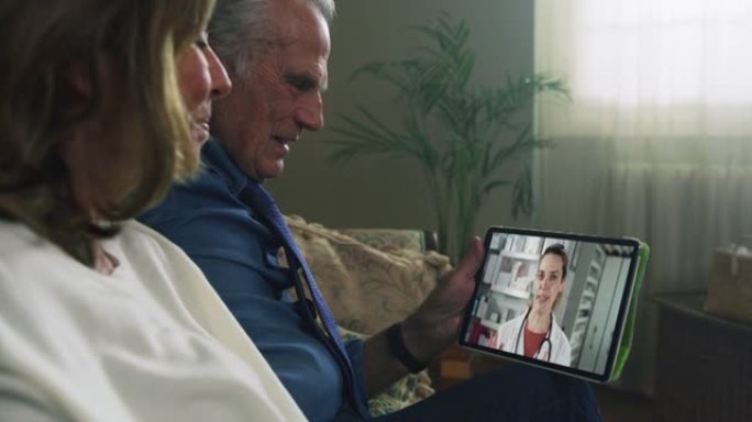 幸福现代成熟的高级夫妇用平板电脑给家庭医生在线咨询的电影镜头。远程健康、远程医疗、在线援助的概念。