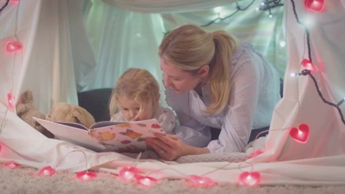 母亲和小女儿在家里孩子卧室的自制营地里读故事