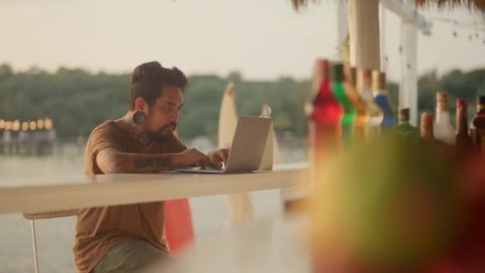亚洲男子使用笔记本电脑在海滩上的酒吧工作。