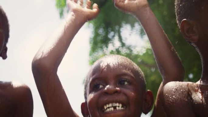 特写一群快乐天真的黑人儿童在长期干旱后玩耍和享受雨水的祝福。当水倒在他们身上时，真正的非洲孩子跳着笑