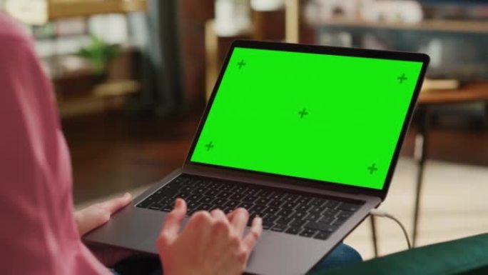 年轻的成年女性在带绿屏模拟显示的笔记本电脑上的家庭阁楼公寓工作。使用触控板和浏览互联网的创意女性。特