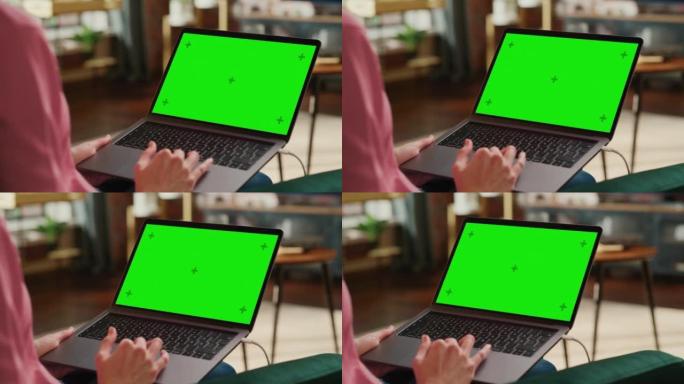 年轻的成年女性在带绿屏模拟显示的笔记本电脑上的家庭阁楼公寓工作。使用触控板和浏览互联网的创意女性。特