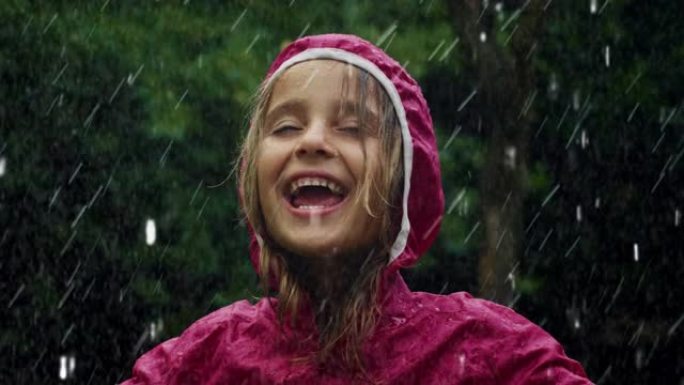 一个穿着粉红色雨衣的快乐小女孩在雨中快乐地站着，被大自然和树木包围着。感恩雨水的祝福，对可持续发展的