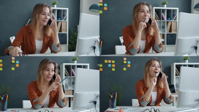 快乐的年轻女子正在办公室的办公桌上用手机讲话，忙于商务对话