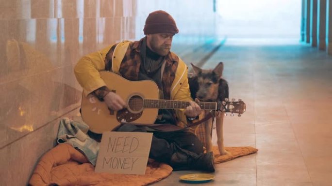 一个无家可归的人正在弹吉他，旁边有一只狗