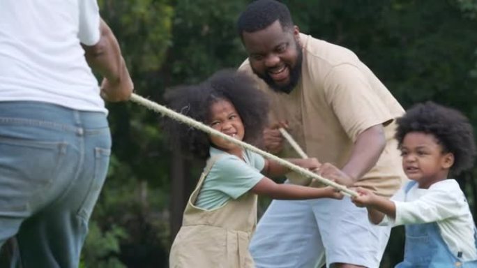 后视图，四个非洲民族家庭的人，年龄在4-5岁的小男孩和小女孩在公园里玩得开心，同时拉绳比赛。野餐概念