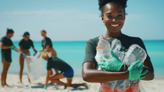 一位年轻的非洲女志愿者的慢动作在镜头前微笑着，对在大海的海滩上捡起塑料垃圾以保护环境感到满意。