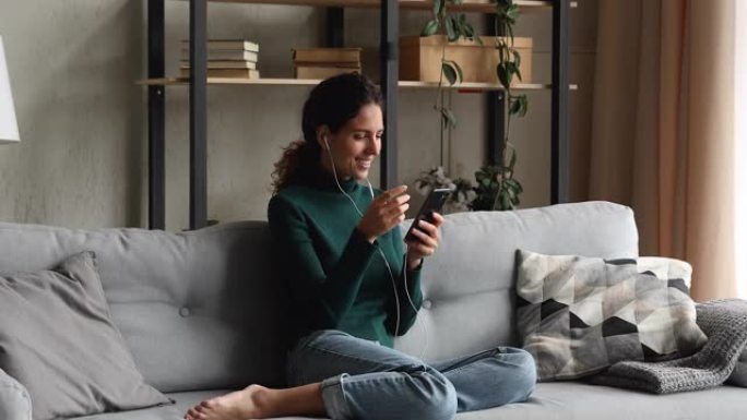 女人在沙发上放松戴有线耳机使用智能手机