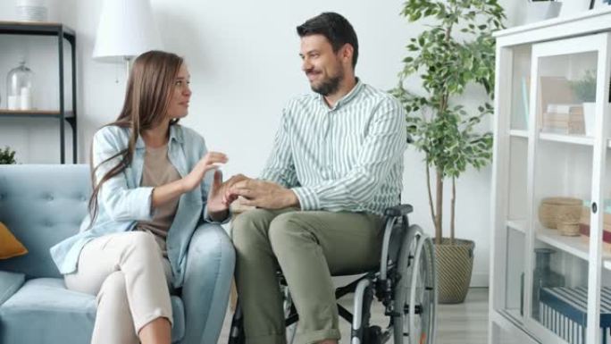 坐在轮椅上的残疾男子在家里与微笑着牵手的女人交谈