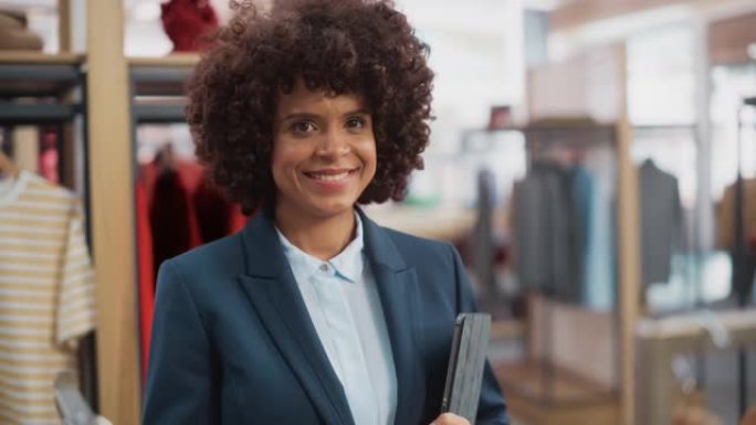 一位快乐的黑人女性肖像，时尚的非洲头发微笑着，在平板电脑的服装店摆姿势拍照。小企业主，担任女商人或销