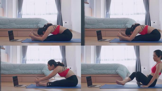 亚洲妇女在卧室里用笔记本电脑在家练习瑜伽