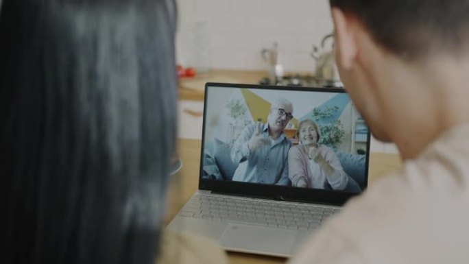 幸福的年轻夫妇在家里使用笔记本电脑进行视频通话时与父母老人交谈的肖像