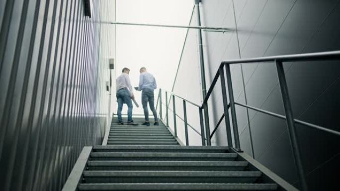 SLO MO两名工程师走上工厂钢走道的楼梯