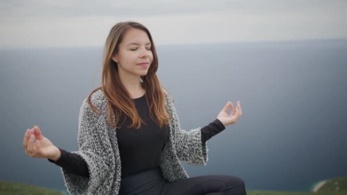 坐在悬崖上的祈祷姿势冥想的年轻女子