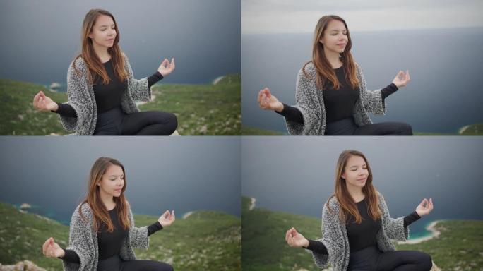 坐在悬崖上的祈祷姿势冥想的年轻女子