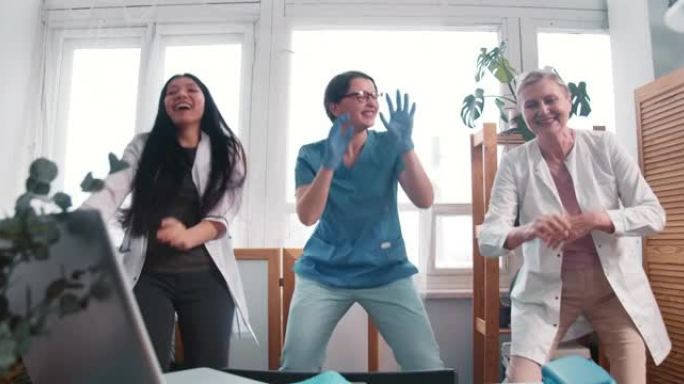 缩小三个有趣的快乐多样化的医生妇女一起跳舞，庆祝在诊所实验室战胜病毒大流行。