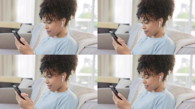 非洲妇女在手机上浏览社交媒体，在耳塞上听音乐，同时在家享受轻松的周末。一位年轻女性坐在客厅里发短信