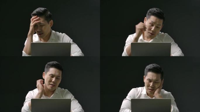 年轻英俊的亚洲男子在使用笔记本电脑工作或在线学习时很累。一个穿着白衬衫，表情严肃的人在隔离期间呆在家