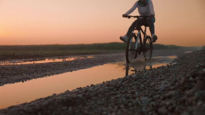 女子骑自行车的人在潮湿的土路上骑自行车