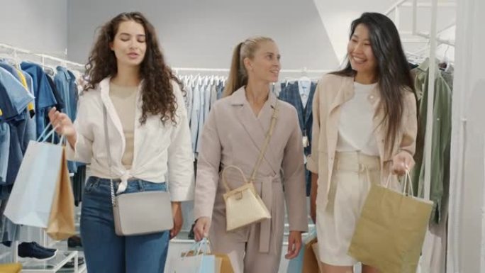 一群年轻妇女走在服装店里，拿着购物袋微笑着说话