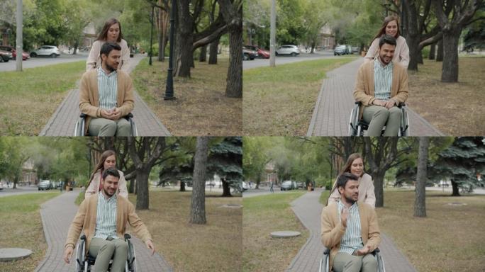在公园里，有爱心的年轻女士推着男人的轮椅在户外微笑着说话的慢动作