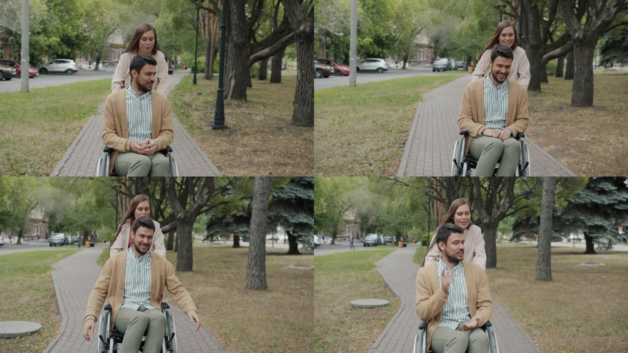 在公园里，有爱心的年轻女士推着男人的轮椅在户外微笑着说话的慢动作