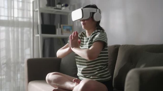 戴着虚拟现实眼镜的女人在家里用荷花姿势冥想，双手在namaste享受模拟和放松