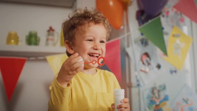 在装饰有气球的厨房里，用泡泡瓶近距离拍摄一个男孩子的肖像。可爱的小男孩吹泡泡，在他的生日聚会上笑。快