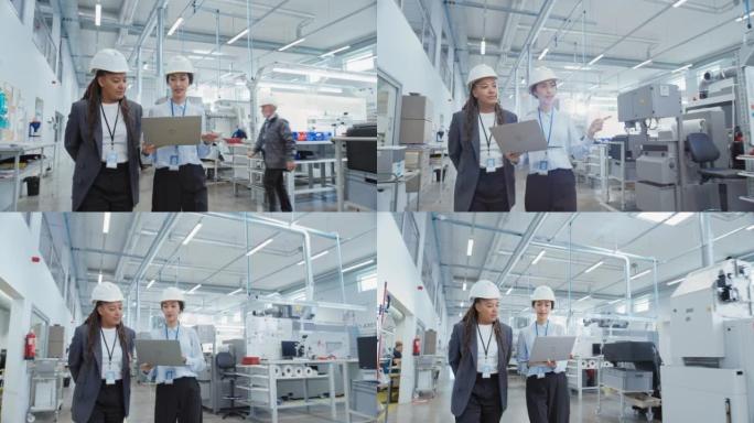 两名女重工业员工在工厂戴着安全帽。步行和讨论工业机器设施，使用笔记本电脑。工作中的亚洲工程师和非裔美