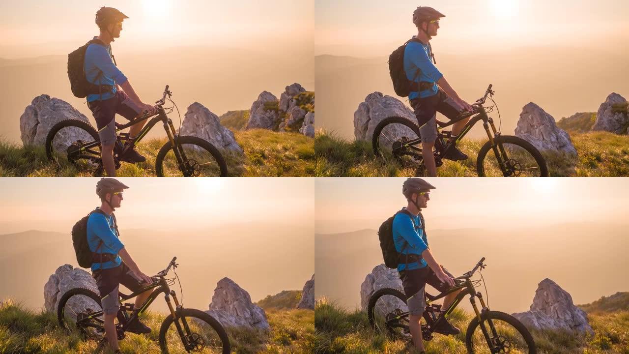 男性山地自行车骑行者站在山的边缘，欣赏日落时的壮丽景色