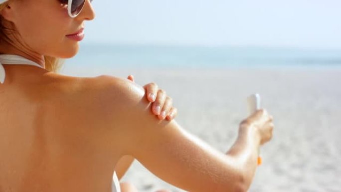4k视频片段，一名妇女在海滩上给自己的身体涂防晒霜