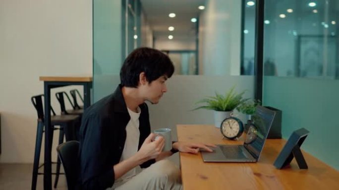 忙碌的亚洲人一边喝咖啡，一边在工作场所的笔记本电脑上看证券交易所。