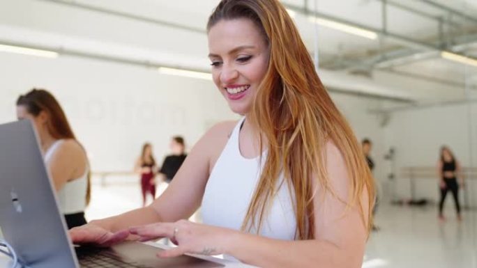 健身教练在舞蹈课休息时使用笔记本电脑