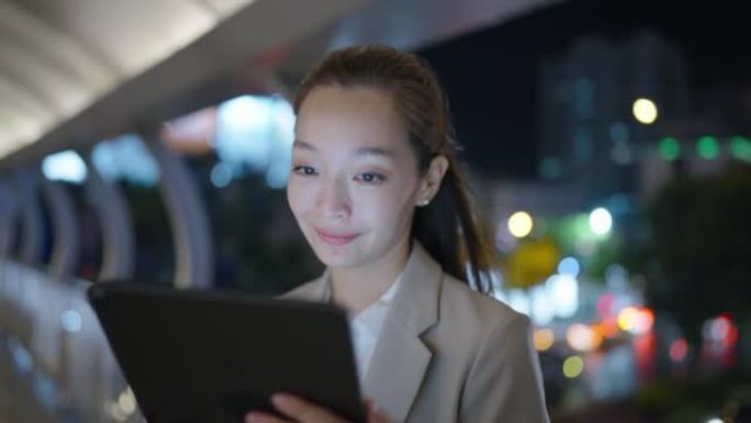 美丽的亚洲女商人在深夜工作时在办公大楼的走廊上行走时在数字平板电脑上工作。商务外景-东南亚/日本概念