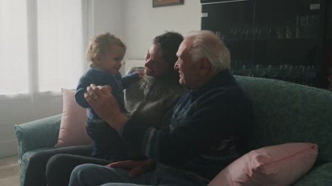幸福家庭的电影镜头: 祖父，女儿和孙子婴儿坐在家里的沙发上，一起度过时光。生活观念，祖父母，世代，童