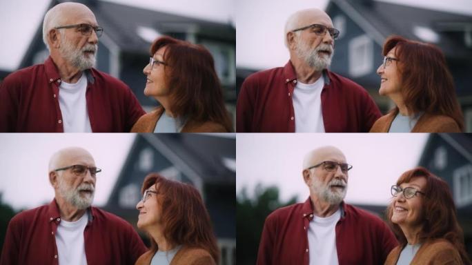 一对幸福的老年夫妇在他们的住宅区家户外摆姿势，互相拥抱的特写肖像。充满爱心的成年人看着镜头微笑，享受