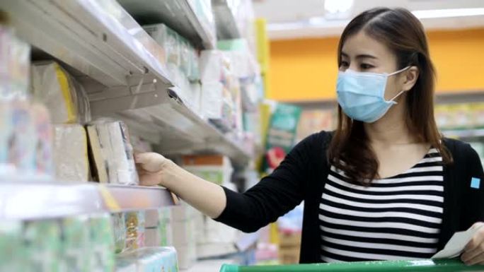 年轻的亚洲妇女带着防护口罩在超市购物，阅读清单