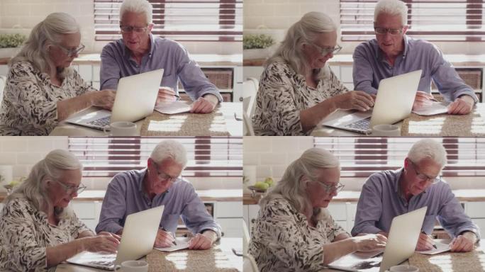 4k视频片段，一对老年夫妇坐在家里的厨房里，使用技术计算他们的财务状况