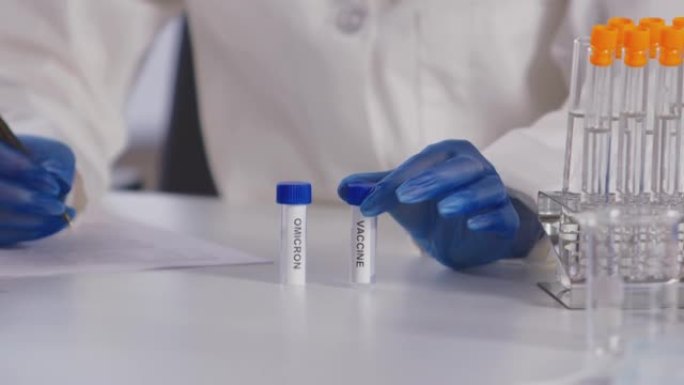 女性实验室研究人员在个人防护用品中研究标有欧米克隆和疫苗的试管