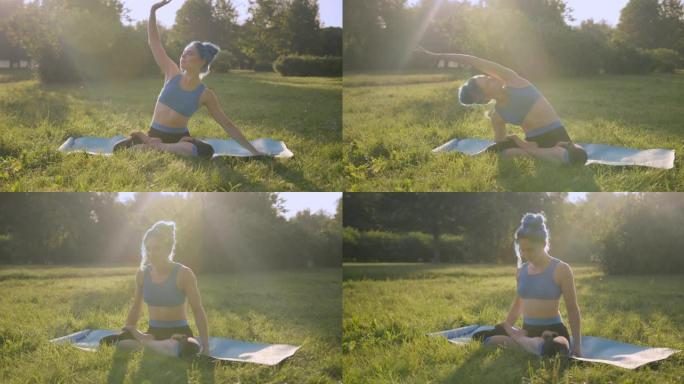 迷人的年轻女子，蓝色的头发，穿着蓝色的瑜伽服装，在公园的草地上做瑜伽，在日出或日落时，左右伸展，在瑜