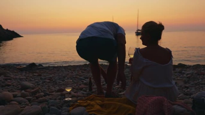 意大利厄尔巴岛日落时，一对夫妇在海滩上喝酒的景色。