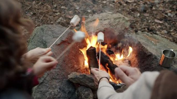 妈妈和儿子烤棉花糖和在火旁玩乐的手的特写