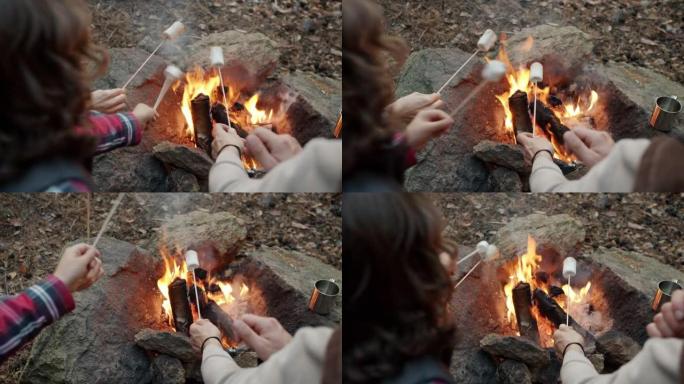 妈妈和儿子烤棉花糖和在火旁玩乐的手的特写