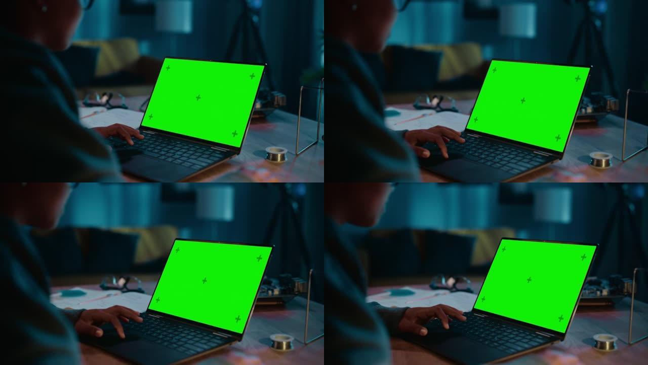 年轻的多种族女孩在家里黑暗舒适的房间里使用带绿屏Chromakey模拟显示的笔记本电脑。她在网上浏览