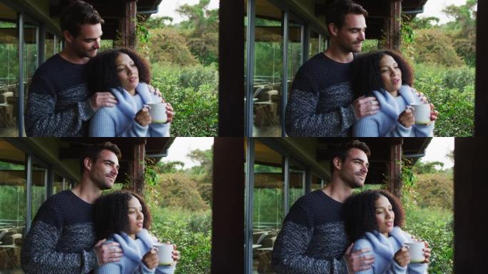 快乐的多元化夫妇站在乡下的阳台上拥抱和喝咖啡