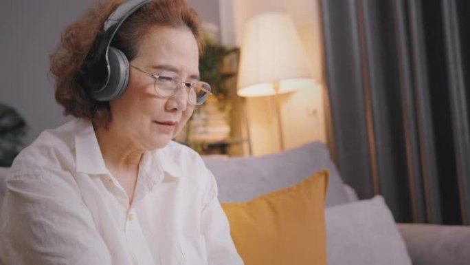 特写镜头亚洲高级女性戴着无线耳机，通过手机听音乐。退休的老年女性，穿着休闲服装，使用智能手机或社交网
