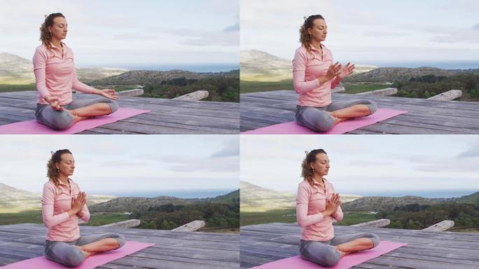 白人妇女坐在乡村山腰的甲板上练习瑜伽冥想