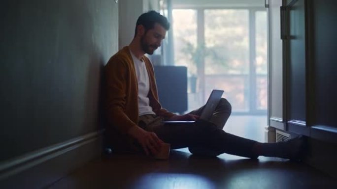 中年男子在家中使用笔记本电脑进行远程工作的肖像。坐在地板上的英俊男子使用互联网，喝早晨的咖啡。丰富的