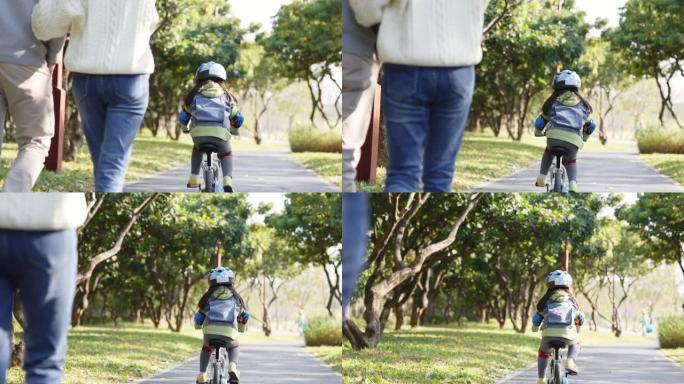 亚洲小女孩在公园骑自行车父母从后面wacing
