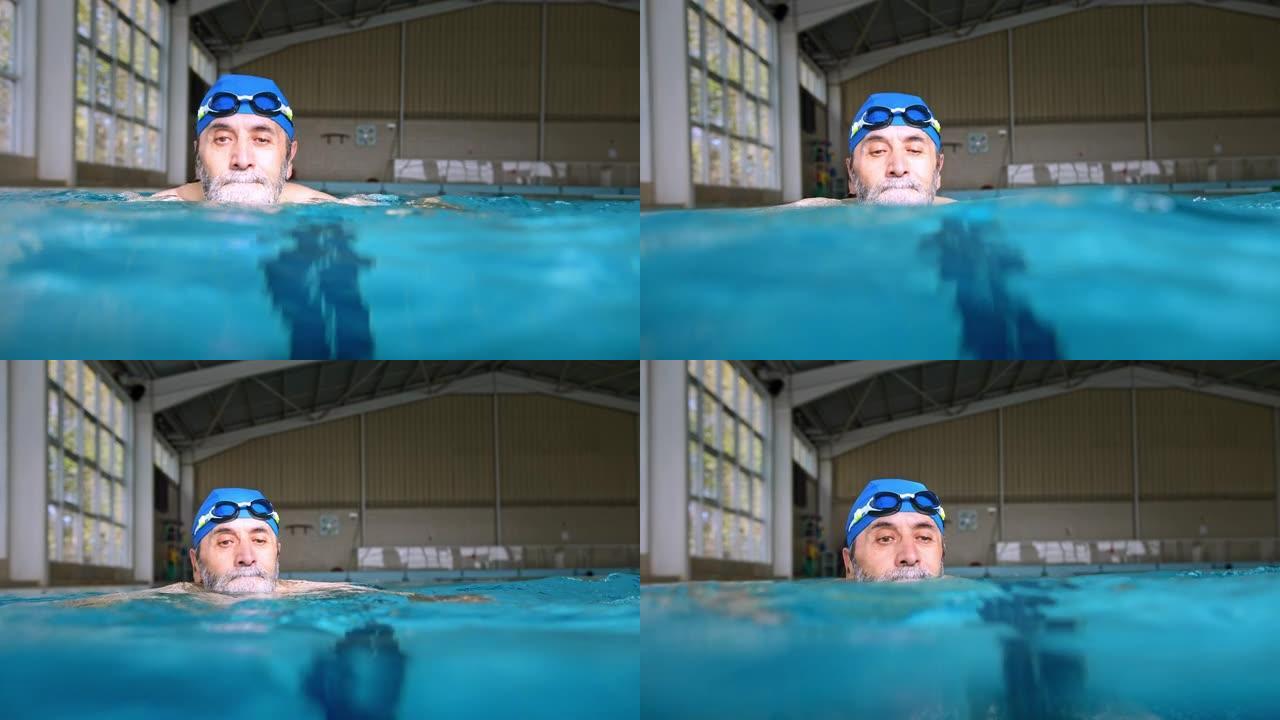 有谷歌和帽子的高级男子在室内游泳池游泳